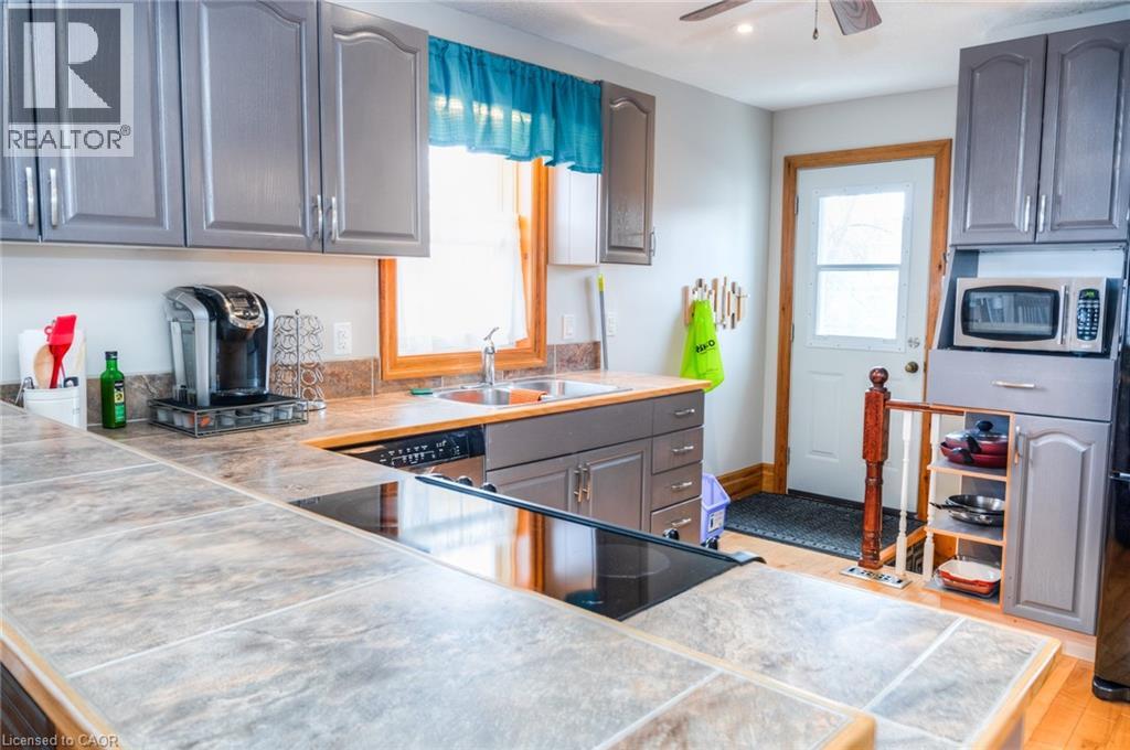 Kitchen featuring grey cabinetry, tile-finish countertops, stainless steel sink, and an integrated cooktop
