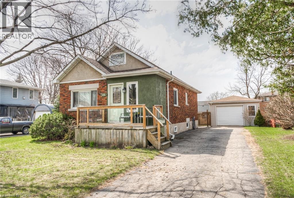 Brick and stucco exterior featuring a front deck with wood railing, a paved driveway, and a detached garage with an overhead door