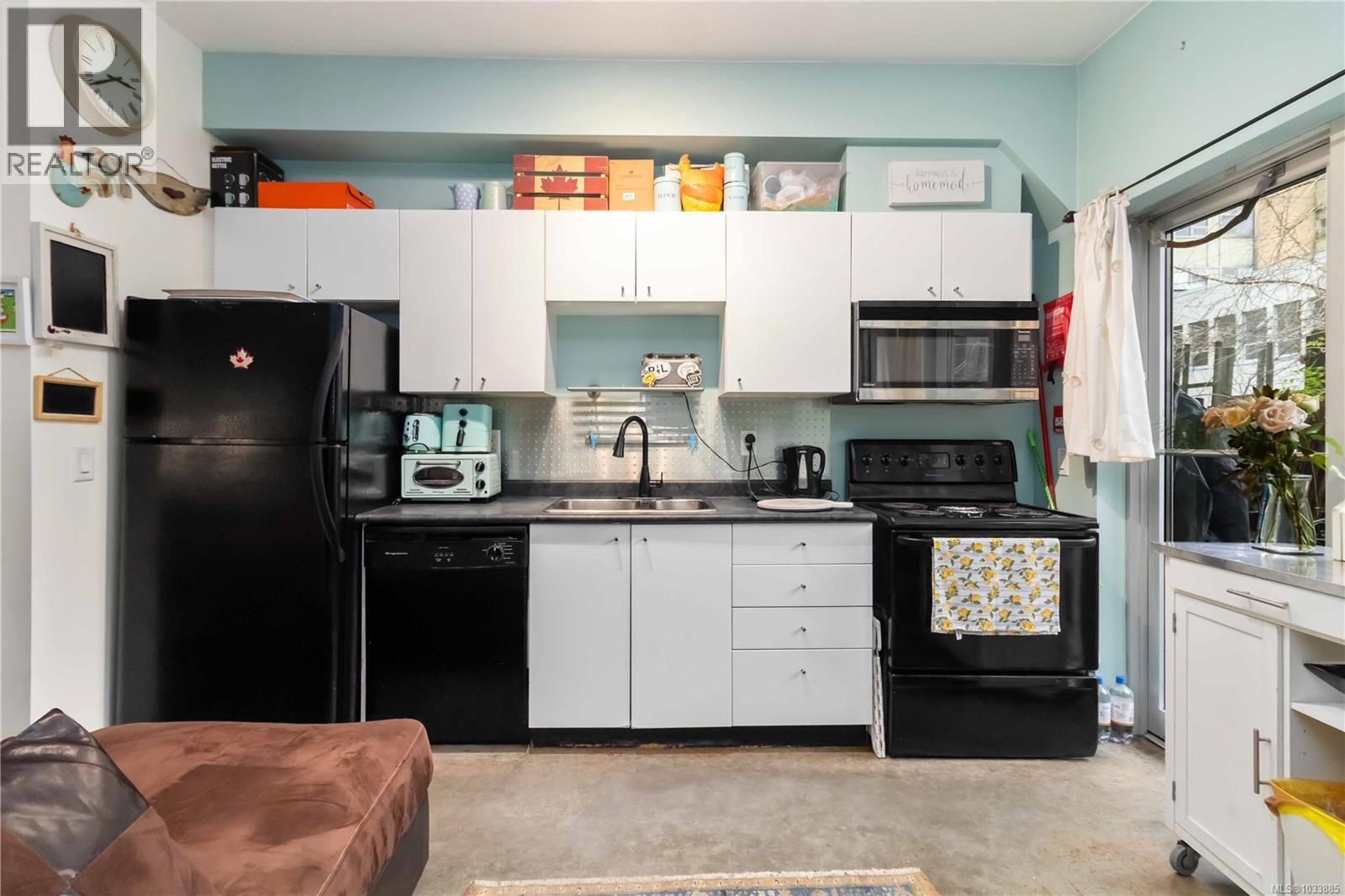 Kitchen with black appliances, white cabinets, dark countertops, concrete flooring, and decorative backsplash
