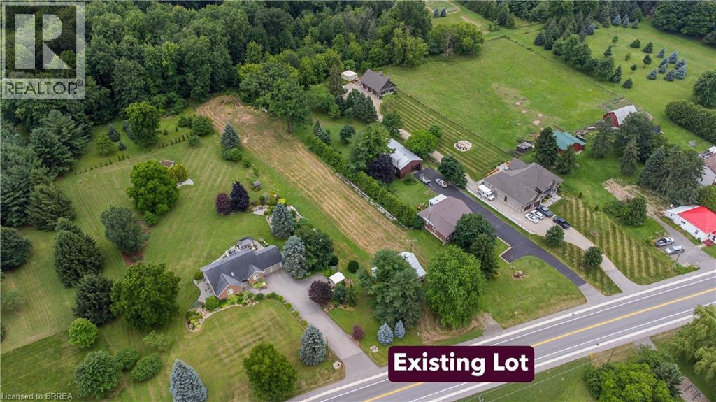 Expansive lot featuring a main residence with a dark shingle roof, extensive green lawns, mature trees, and a paved driveway