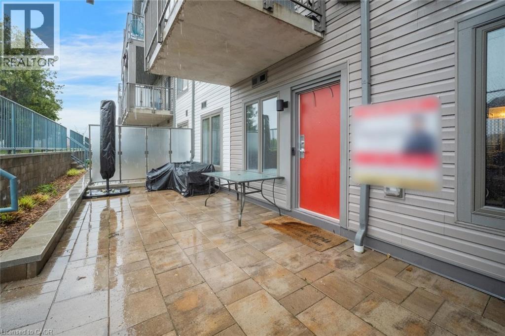 Spacious patio featuring a stone paver surface, a vibrant red entry door, horizontal siding, and a glass privacy screen