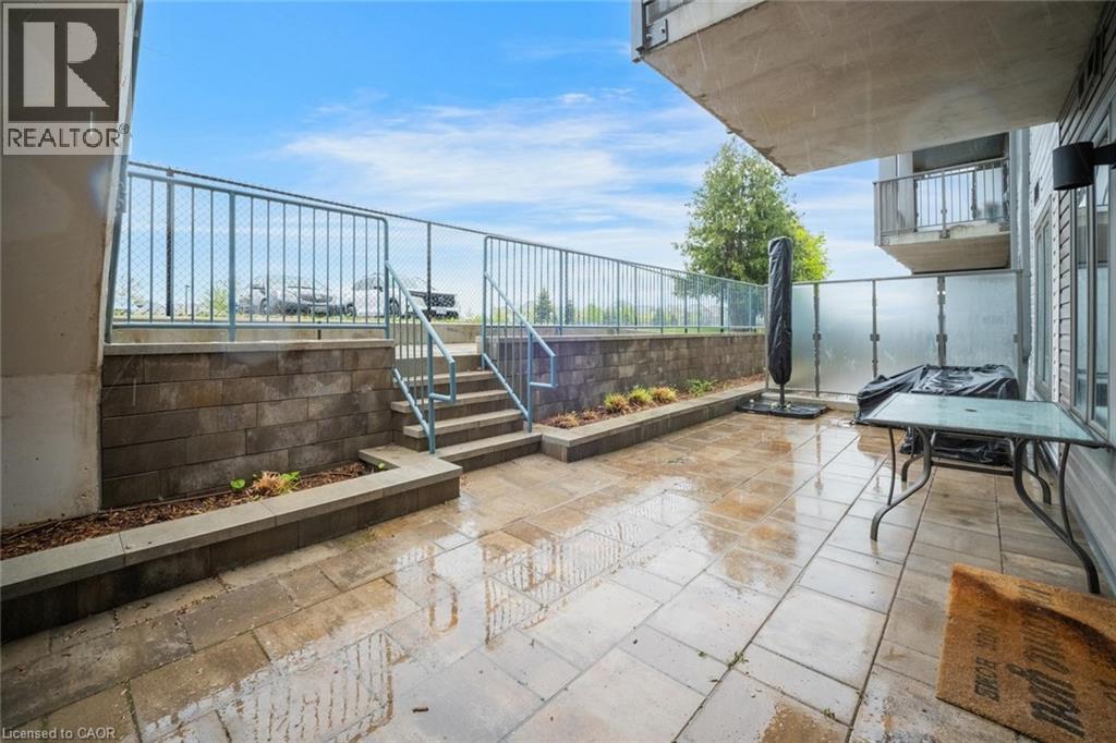 Spacious outdoor patio featuring stone paver flooring, a raised garden bed with retaining wall, and a metal railing
