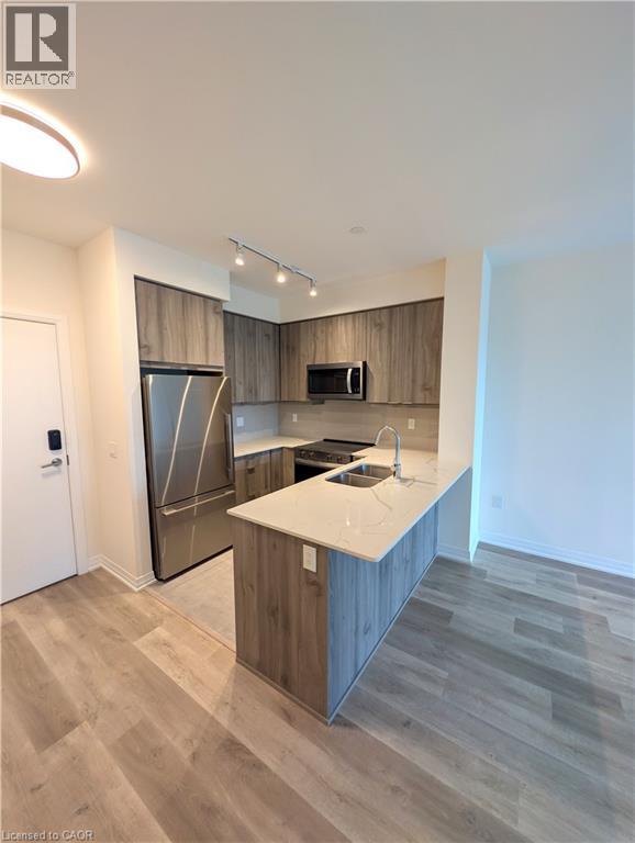 Modern kitchen featuring wood-finish cabinetry, stainless steel appliances, a white countertop island with an undermount sink, and wood-finish flooring