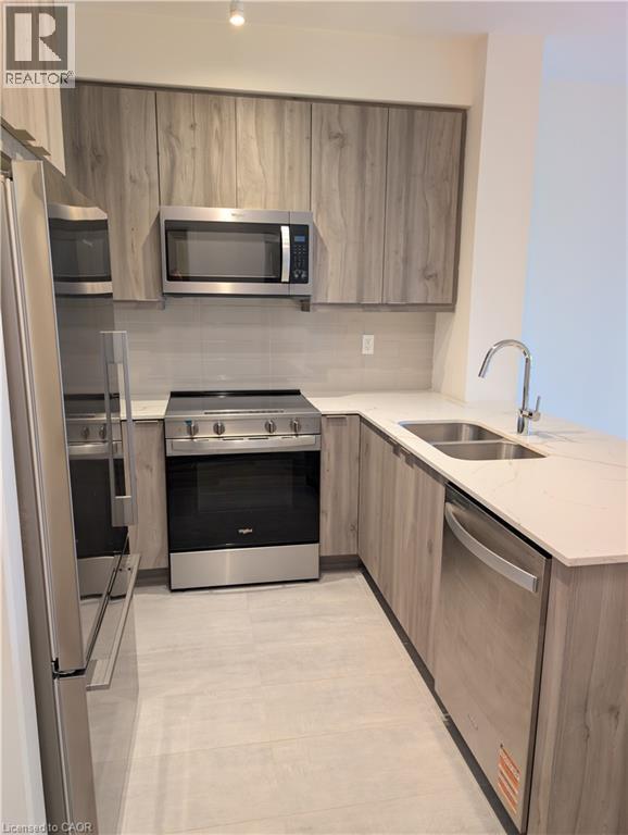 Modern kitchen featuring wood-finish cabinetry, stainless steel appliances, a double basin sink, light-toned countertops, and a subway tile backsplash