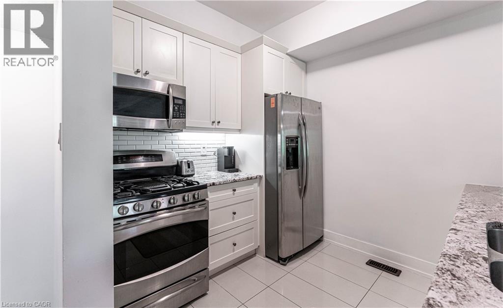 Kitchen featuring white shaker-style cabinetry, stainless steel appliances, granite countertops, a subway tile backsplash, and light-toned tile flooring