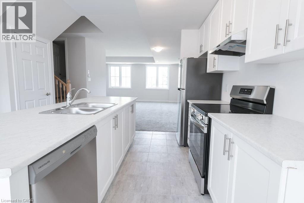 Kitchen featuring white cabinetry with brushed nickel hardware, a stainless steel double basin sink, and integrated stainless steel appliances including a dishwasher, refrigerator, and range