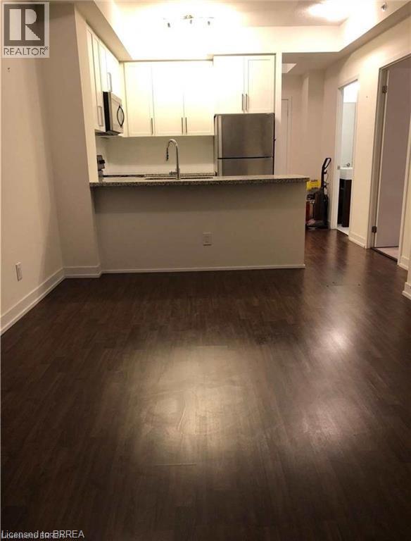 Open-concept living area featuring rich wood-finish flooring, a kitchen with white cabinetry, stainless steel appliances, a granite-look countertop, and a breakfast bar