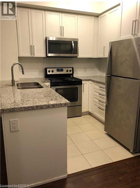 Kitchen featuring white shaker-style cabinetry, light-toned granite countertops, stainless steel appliances, a stainless steel undermount sink with a gooseneck faucet, and light-toned square floor til