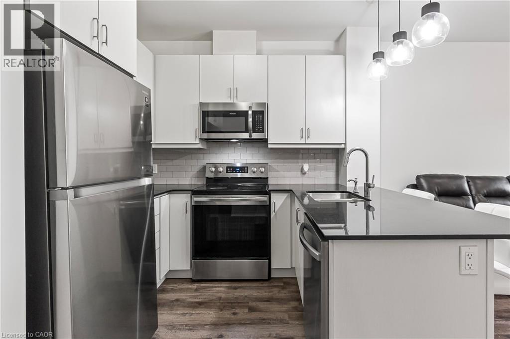 Kitchen featuring stainless steel appliances, a peninsula, dark countertops, dark wood-style flooring, and white cabinets