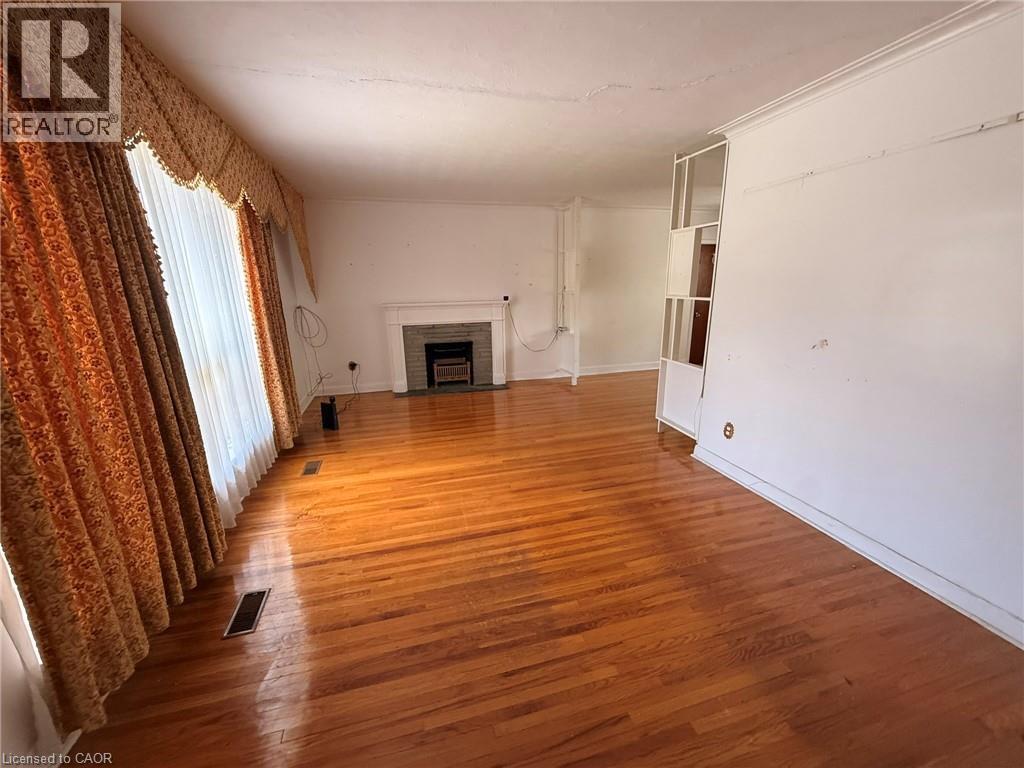 Spacious interior room featuring wood-finish flooring, a white mantel fireplace with a dark-toned firebox, and a large window with draped treatments