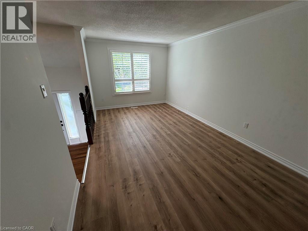 Spacious room featuring wood-finish flooring, crisp white walls, and a large window with plantation shutters