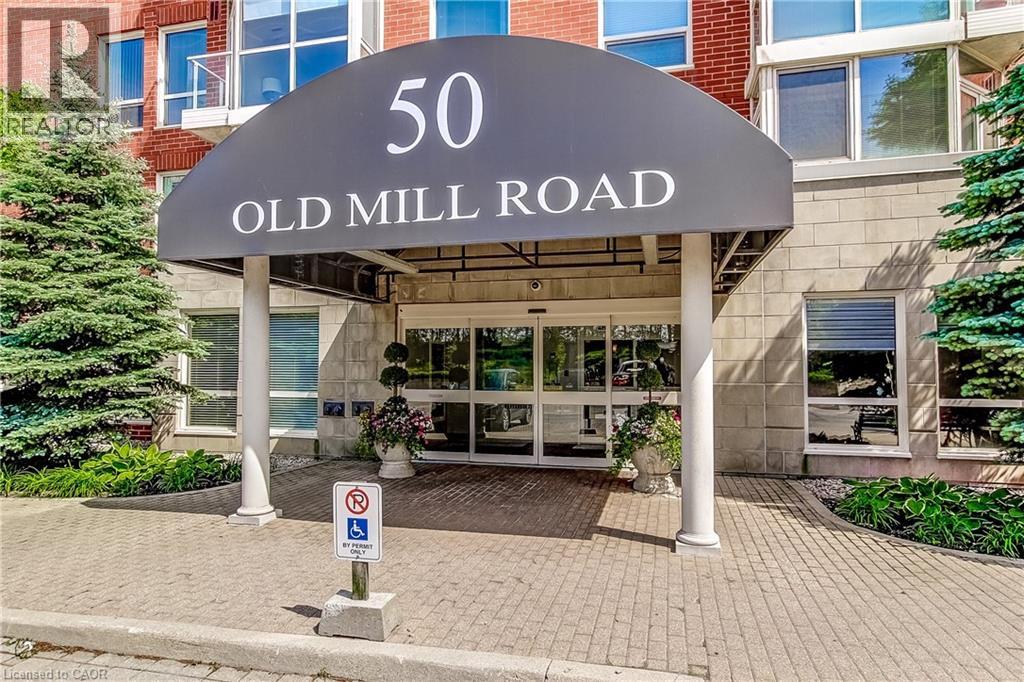 Welcoming building entrance featuring a dark awning, automatic glass doors, brick and stone facade, and mature evergreen landscaping