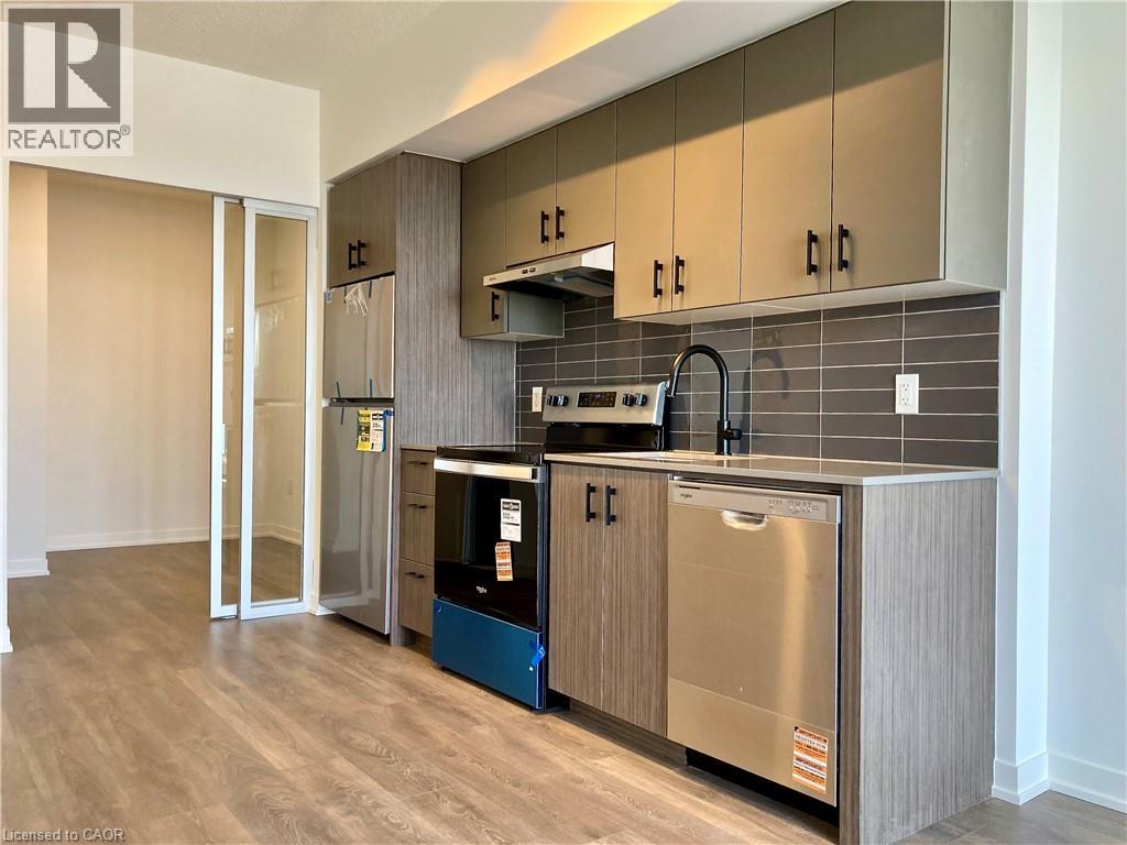 Contemporary kitchen featuring wood-finish flooring, stainless steel appliances, dark subway tile backsplash, matte black faucet, and two-tone cabinetry with dark hardware