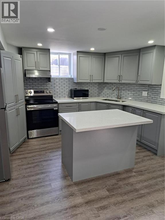 Contemporary kitchen featuring light gray cabinetry, white countertops, a subway tile backsplash, and wood-finish flooring
