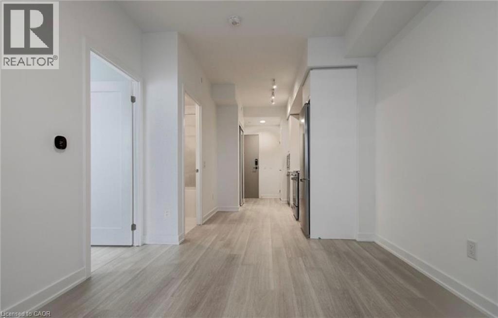 Open-concept room featuring light wood-finish flooring, white walls, and a modern kitchen area with stainless steel appliances
