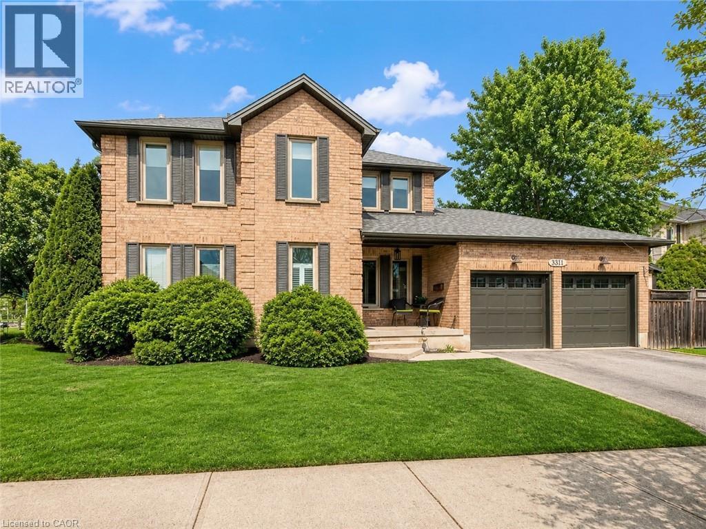 Brick two-story residence featuring a dual garage, gabled roofline, and established landscaping