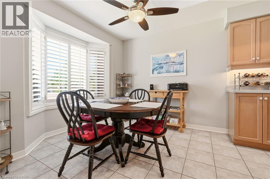 Bay window with plantation shutters, tile flooring, wood-finish cabinetry, and a ceiling fan