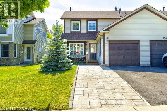 Beige siding exterior with brown trim, featuring a paved driveway and an interlocking stone walkway