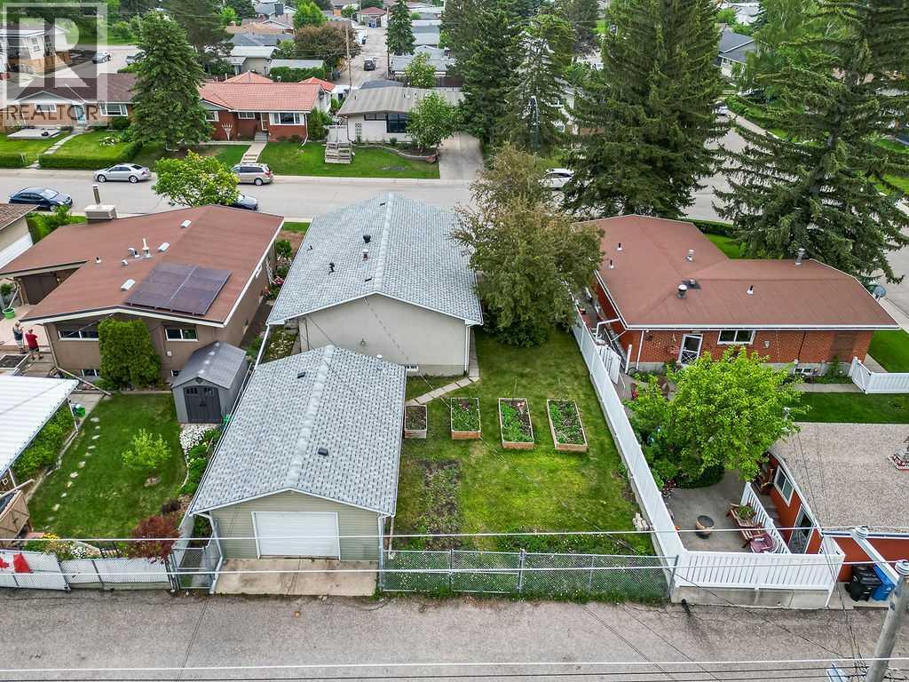 A bird's-eye view showcases the generous lot size, raised garden beds, oversized garage, and expansive backyard space