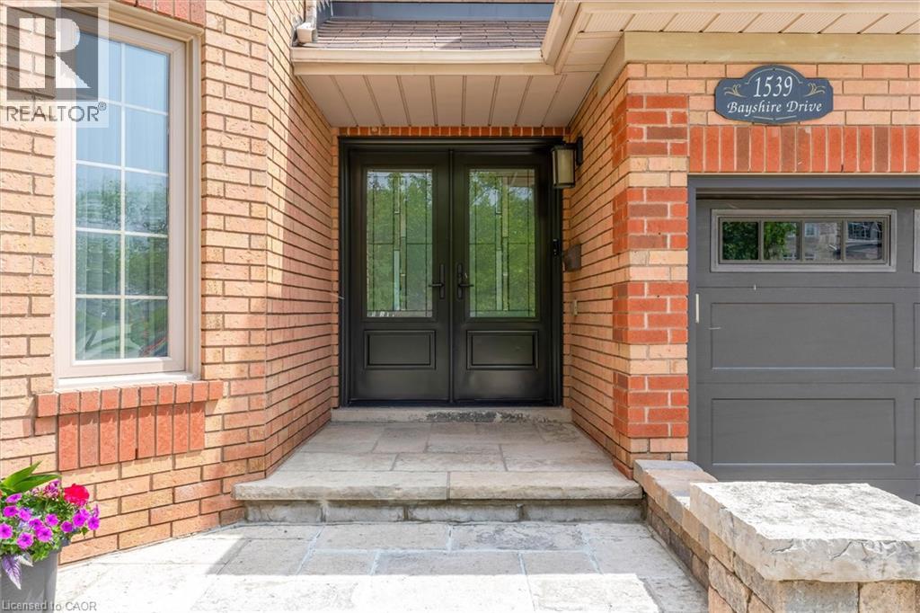 Brick exterior featuring a double-door entry with decorative glass, a single-pane window with grid inserts, a gray garage door with a window panel, stone steps, and an exterior wall lantern