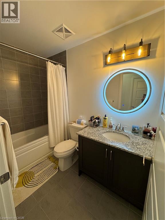 Bathroom featuring a dark wood-finish vanity with a granite-style countertop, an oval mirror with integrated lighting, and a bathtub with gray tiled surround