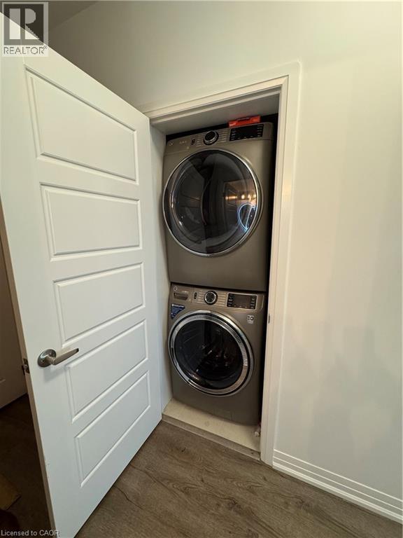 Dedicated laundry closet featuring a stacked washer and dryer, wood-finish flooring, and a paneled interior door