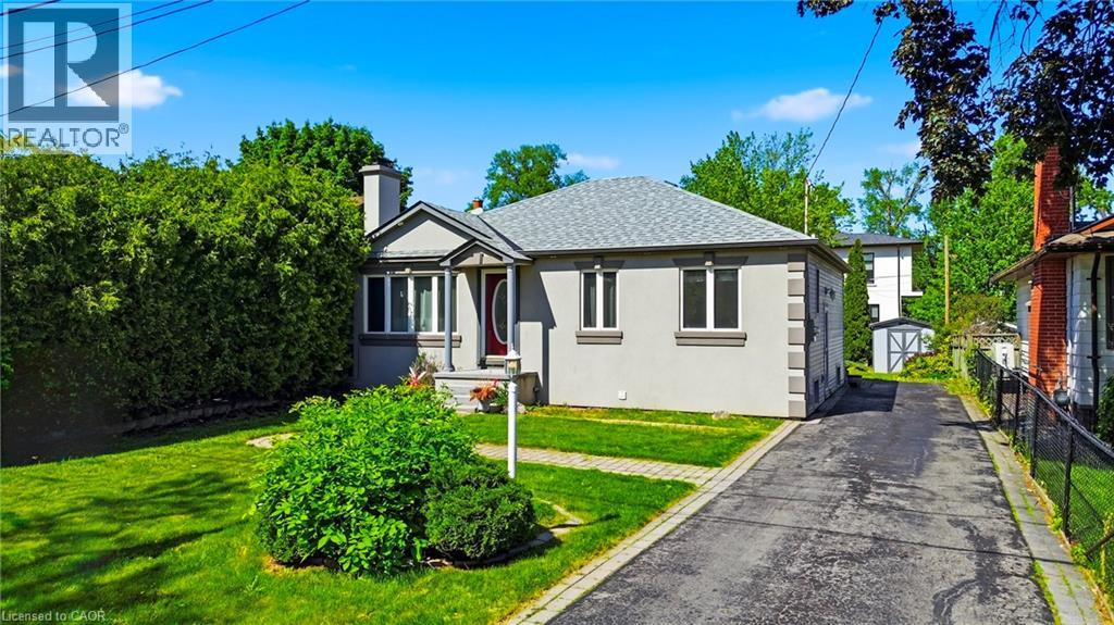Bungalow exterior featuring a gray stucco finish, bay window, red entry door, and a shingle roof
