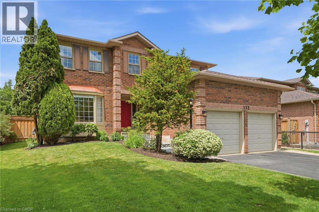 Brick exterior with an attached two-car garage, manicured lawn, and mature landscaping