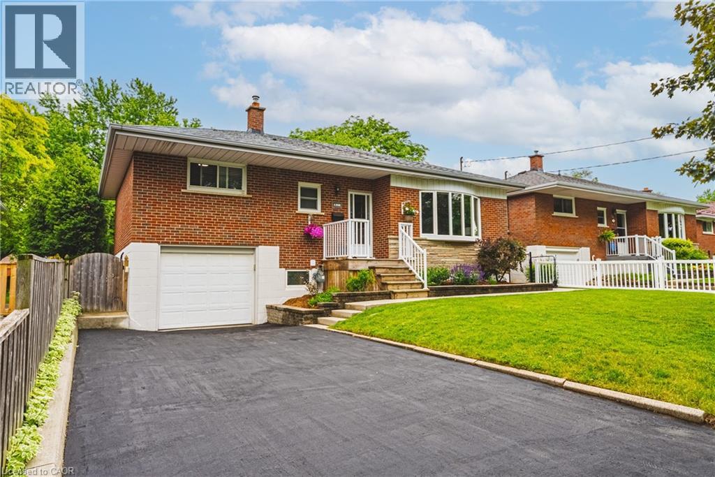 Brick exterior home featuring a bay window, white railings, mature landscaping, an attached garage, and an asphalt driveway