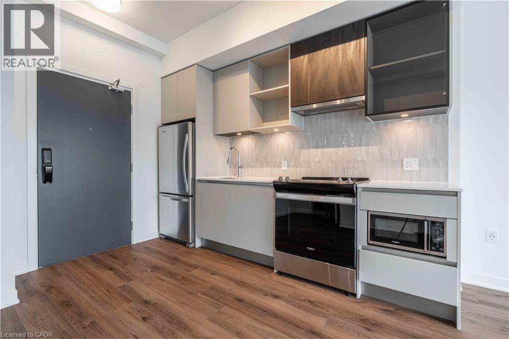 Contemporary kitchen space with wood-finish flooring, stainless steel appliances, light gray flat-panel cabinetry, white solid surface countertops, and a full tile backsplash