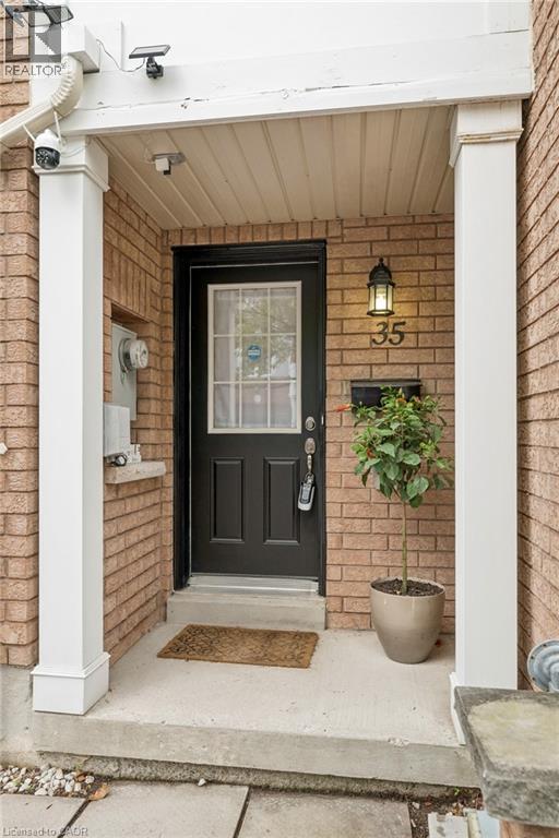 Brick exterior featuring a covered entryway with white support columns, a black front door with a window pane, an exterior wall sconce, and house number ""35""