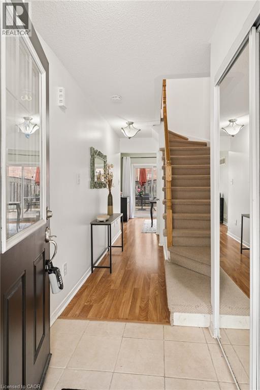 Entryway featuring ceramic tile flooring, wood-finish flooring extending into the interior, a carpeted staircase with wood handrails, and a full-height mirrored sliding closet door