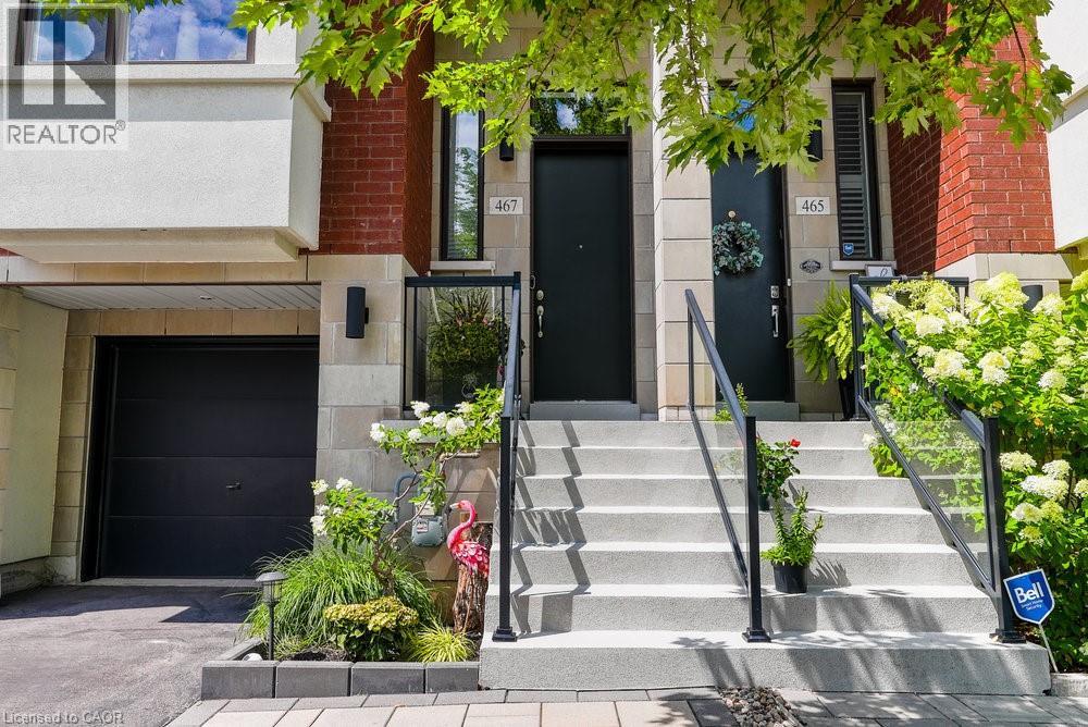 Modern townhome exterior featuring a black garage door, stone and brick facade, front entry stairs with glass railings, and landscaping