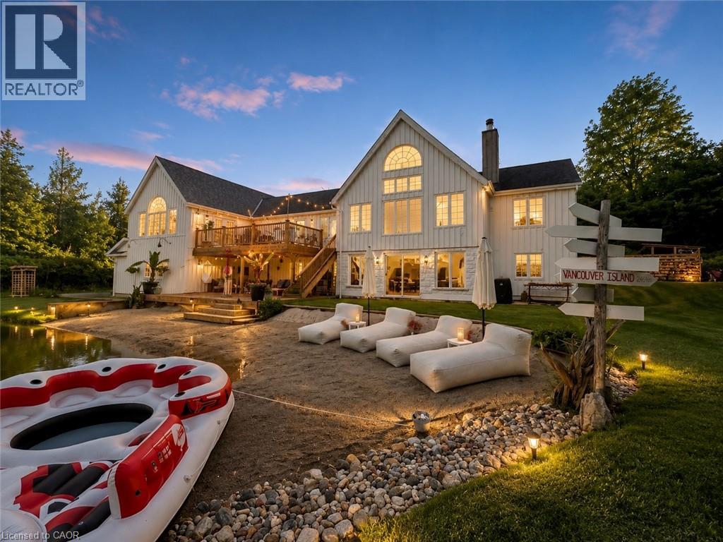 White vertical siding exterior with a multi-level wood deck, ground-level patio, and a sandy beach area