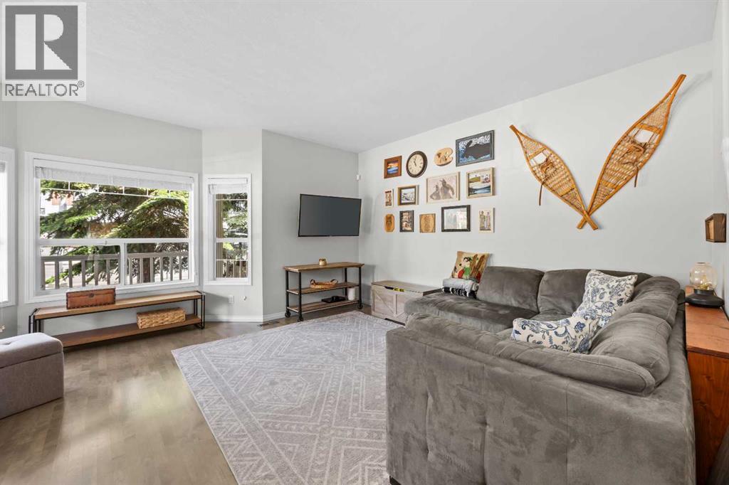 A comfortable front family room bathed in natural light from oversized windows, with rich hardwood underfoot