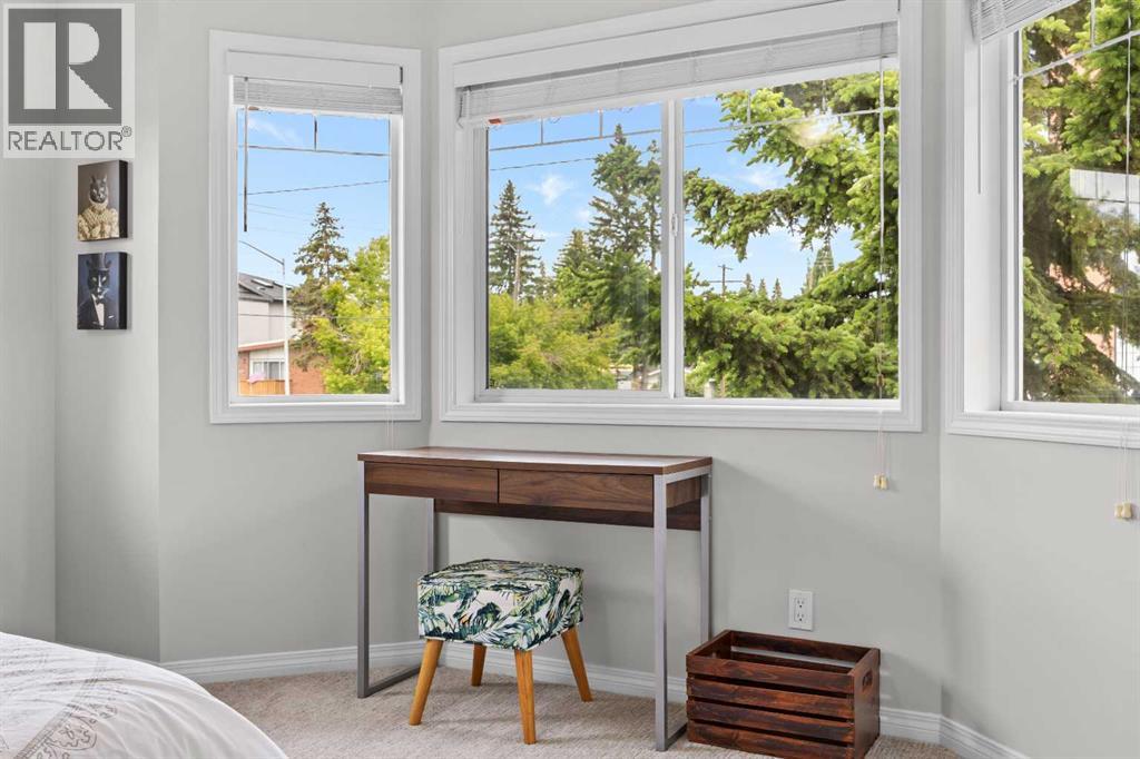 A peaceful corner sitting nook in the primary bedroom, framed by bright windows and treed neighbourhood views