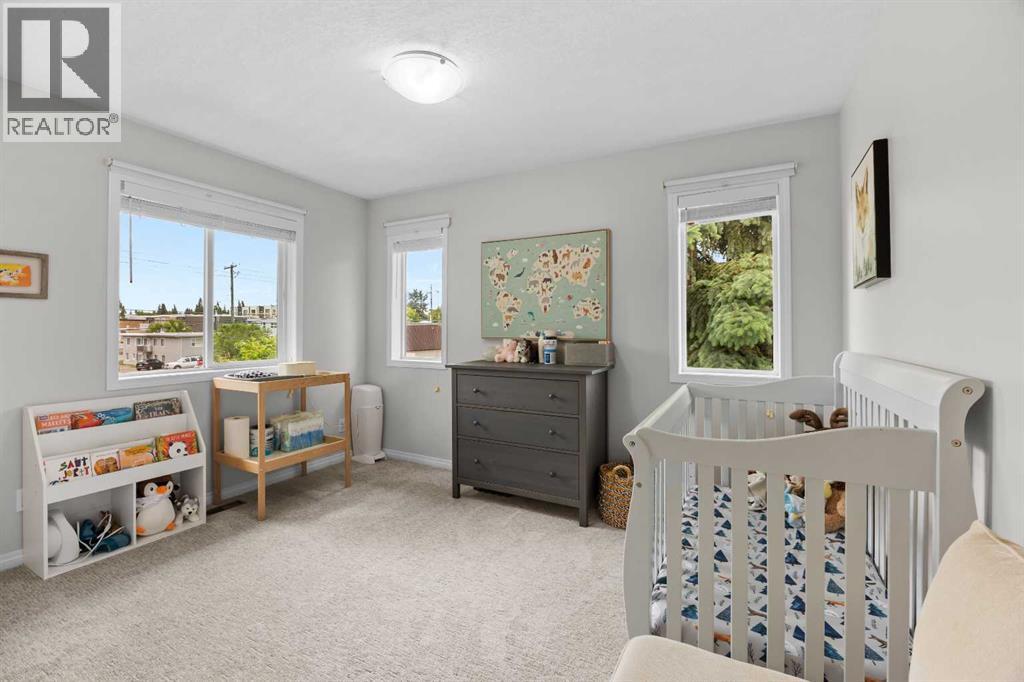 A bright second bedroom set up as a nursery, with two sunny windows and treed outlooks