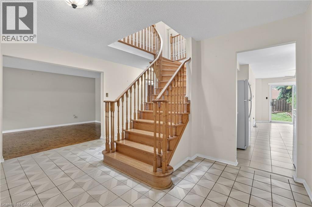 Entryway featuring a curved wooden staircase with turned spindles, patterned tile flooring, and an open archway to a room with wood-finish flooring