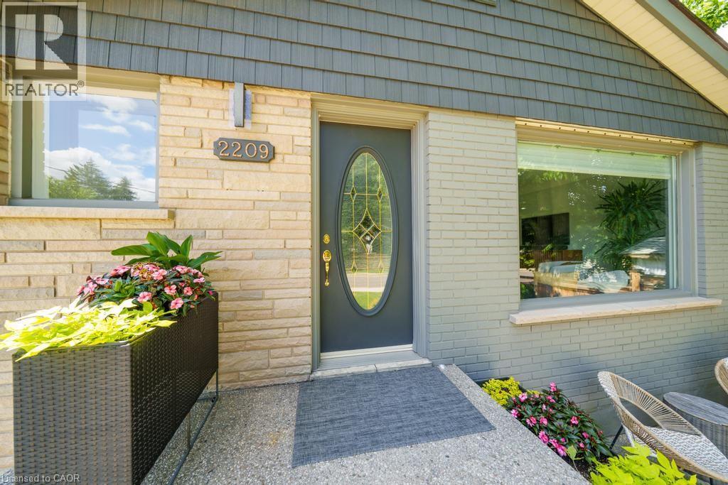 Exterior featuring a leaded glass oval entry door, light-toned stone facade, gray painted brick, large picture window, and shake siding