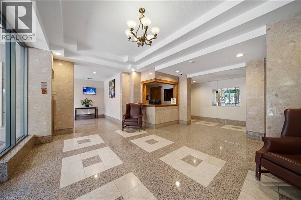 Lobby featuring stone-finish flooring with inset lighter square patterns, stone-clad walls, and a recessed ceiling with a brass-finish chandelier