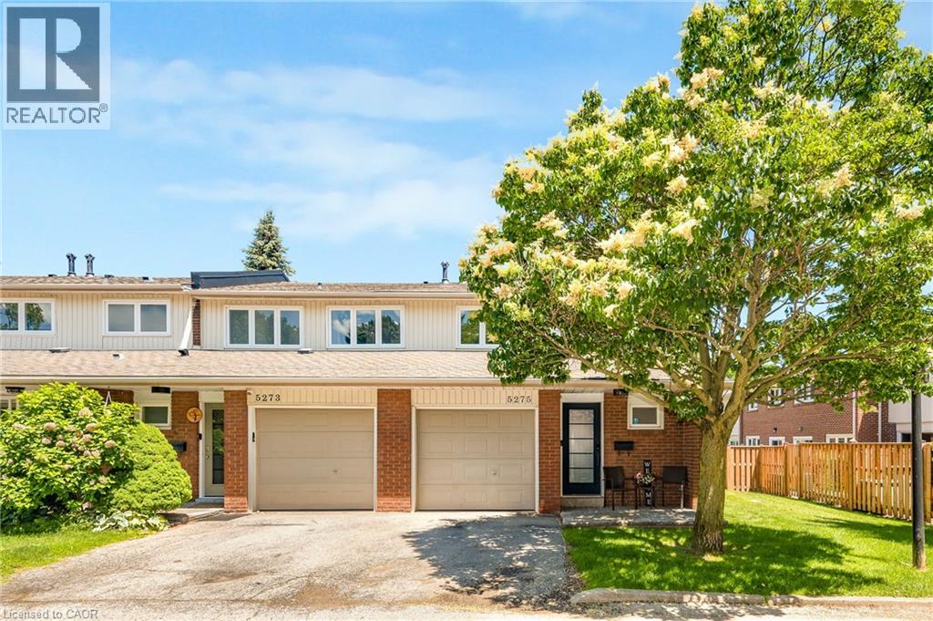 Brick and siding townhome featuring an attached single-car garage, mature front yard tree, and front entry porch with an exterior light fixture