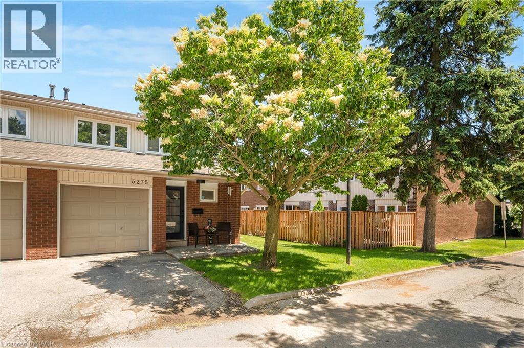 Brick and siding townhouse exterior featuring a single-car garage, front entry with a transom window, paved driveway, and mature landscaping