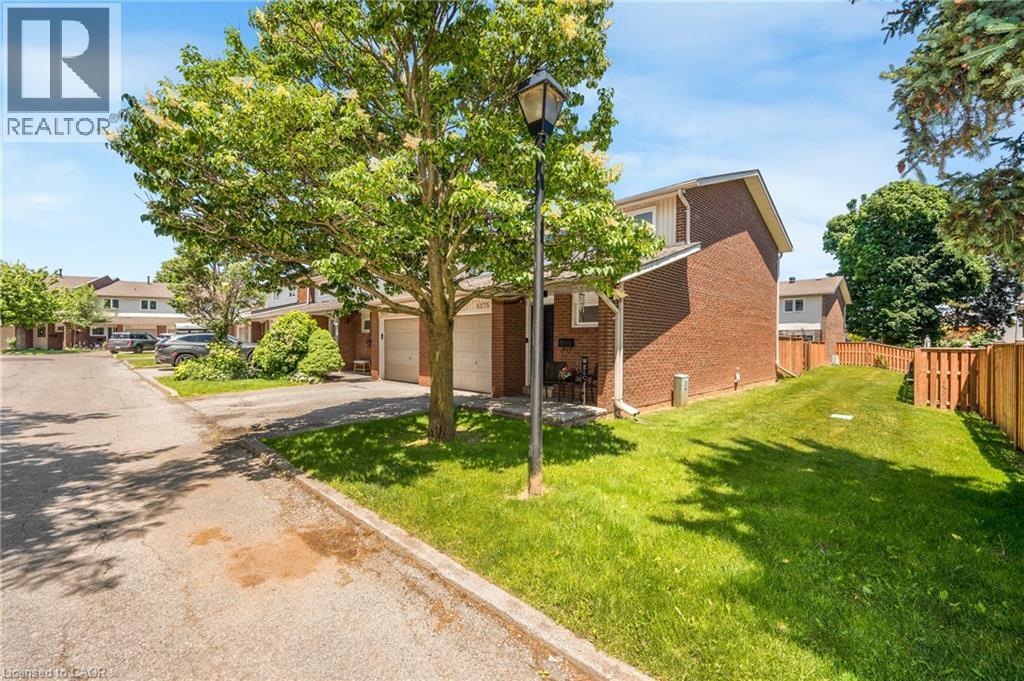 Brick exterior residence featuring an attached garage, a private driveway, a fenced yard, and mature trees