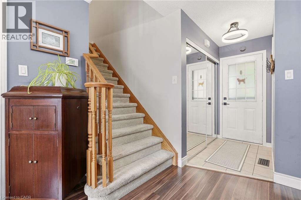 Entryway featuring a carpeted staircase with wood banister, wood-finish flooring, and a tiled landing