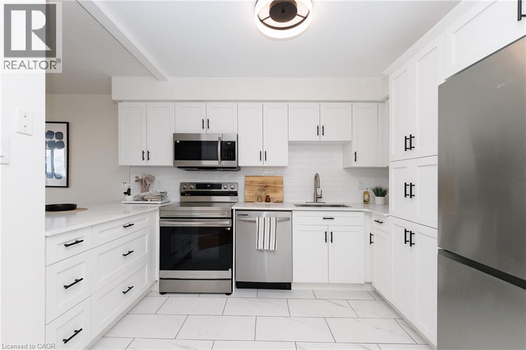 U-shaped kitchen featuring white shaker cabinetry with matte black hardware, stainless steel appliances, a white subway tile backsplash, and light-toned countertops