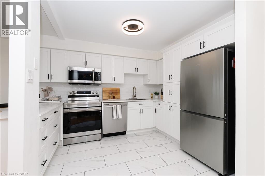 Modern kitchen featuring white cabinetry, stainless steel appliances, light-toned countertops, a subway tile backsplash, and large format floor tiles