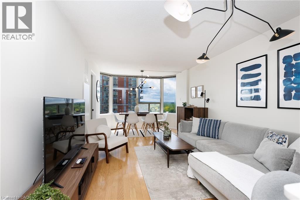 Open-concept living area with light wood-finish flooring, white walls, a modern ceiling light fixture, and a bay window