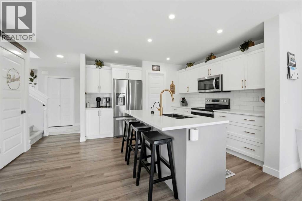 The bright kitchen has white cabinetry, gold hardware, quartz countertops, subway tile backsplash, a centre island with a gold faucet, upgraded stainless steel appliances, and a pantry