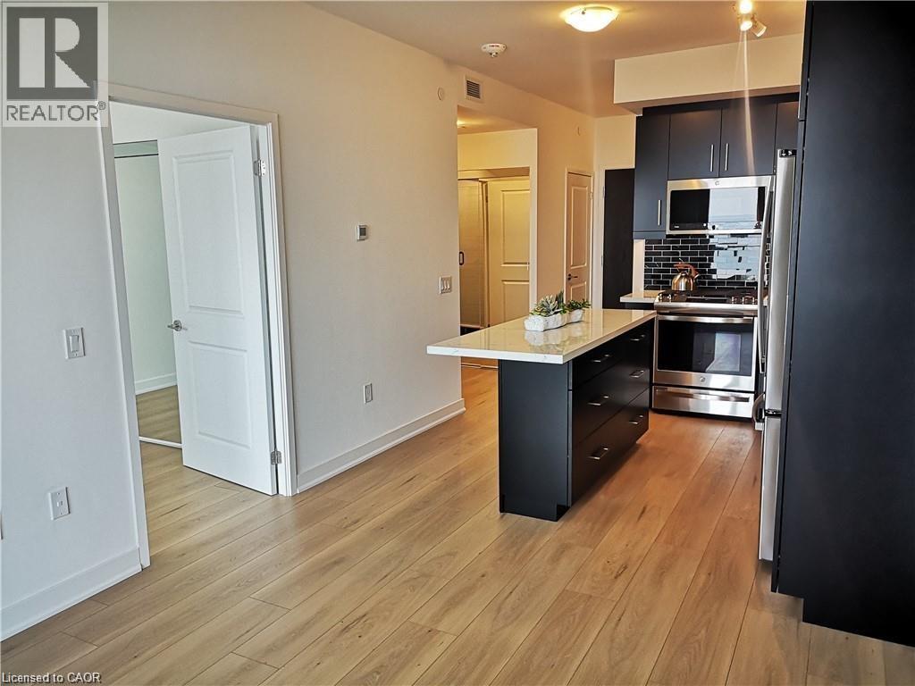 Modern kitchen featuring dark cabinetry, stainless steel appliances, a black subway tile backsplash, and a central island with a light-toned countertop