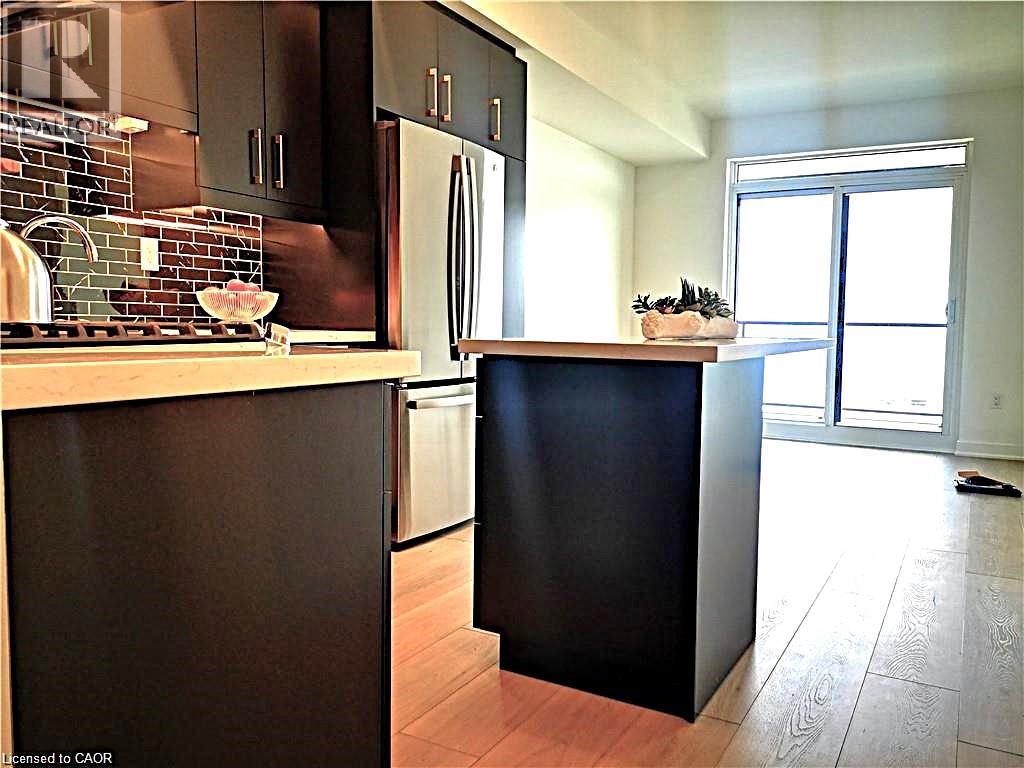 Contemporary kitchen featuring dark flat-panel cabinetry, light-toned countertops, and a mosaic tile backsplash
